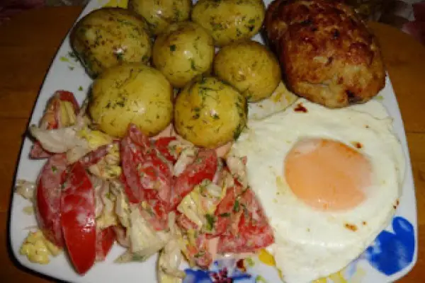 Kotlet mielony, jajko sadzone, młode ziemniaki i surówka z pomidorów i sałaty.