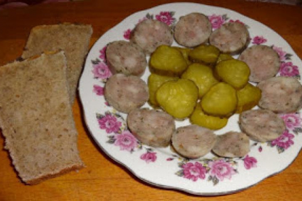 Domowa, biała kiełbasa, parzona oraz marynowany ogórek.